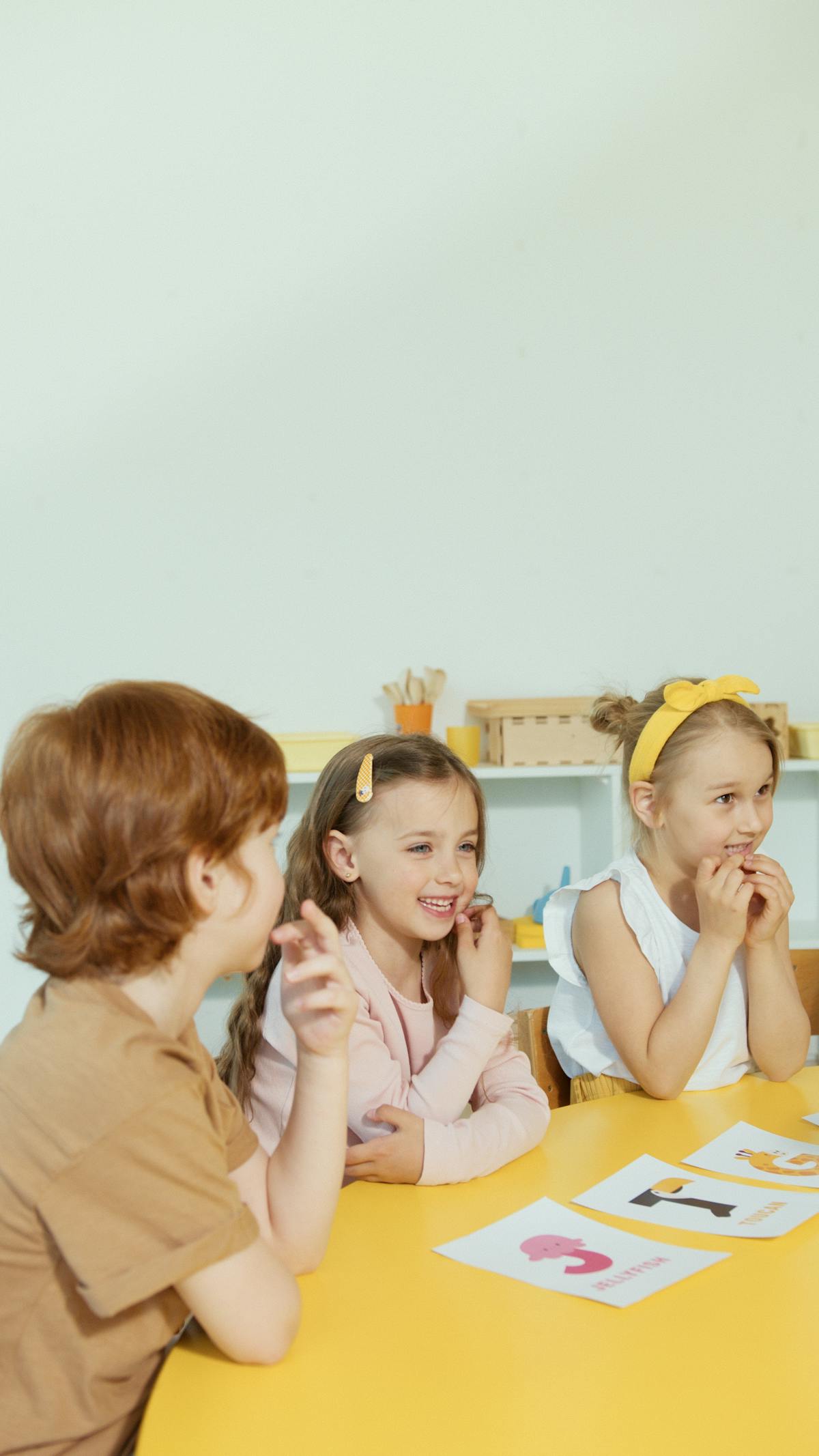 Three children smiling and learning together at a table with flashcards